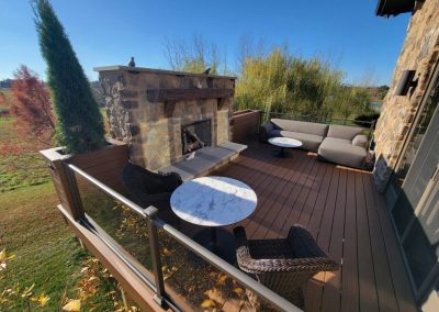 Composite deck build with outdoor stone fireplace and glass railings